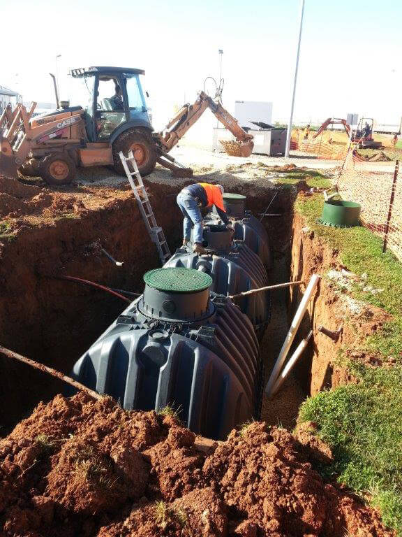 A large trench has been dug into a grassed area, inside a GRAF Carat water tank is being installed. A worker in high visibility clothing standing on the tank and a forklift can be seen in the background.